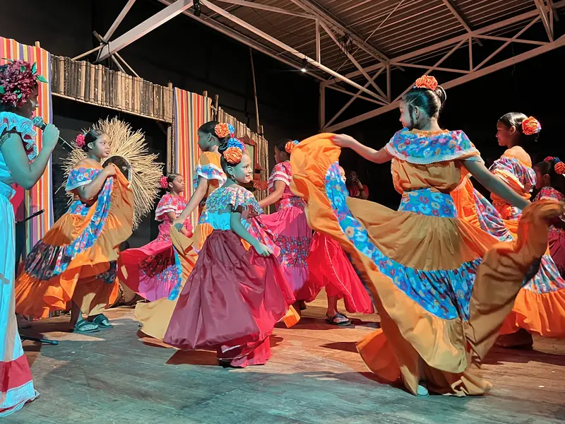 Girls from several groups dancing together in polleras of different colors.